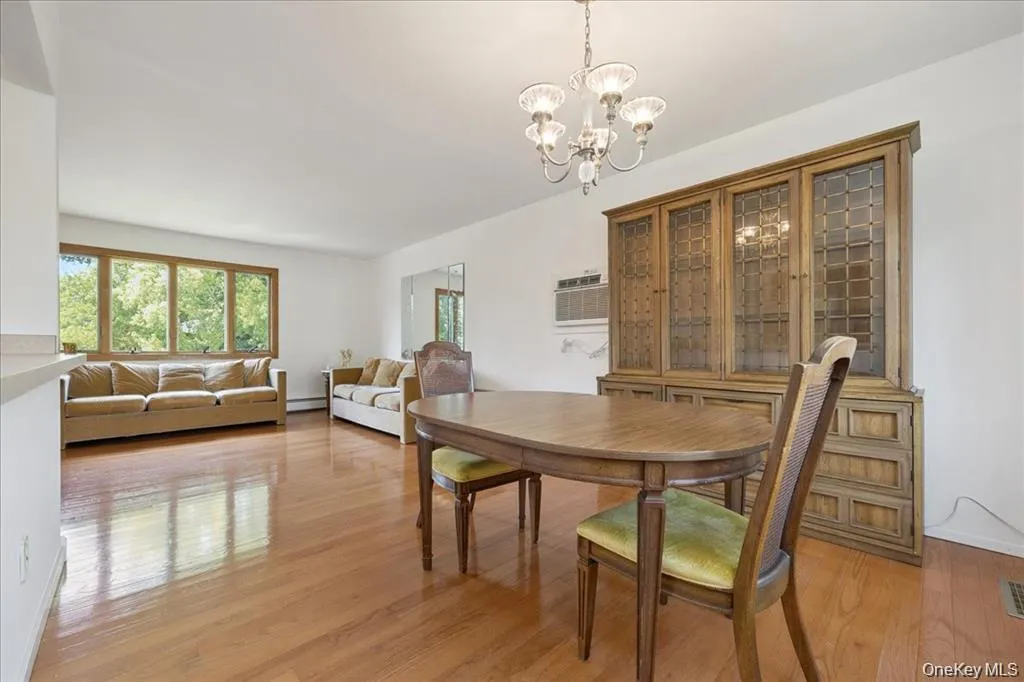 Dining area with a chandelier, light wood-type flooring, and a wall mounted AC Dining area with a chandelier, light wood-type flooring, and a wall mounted AC