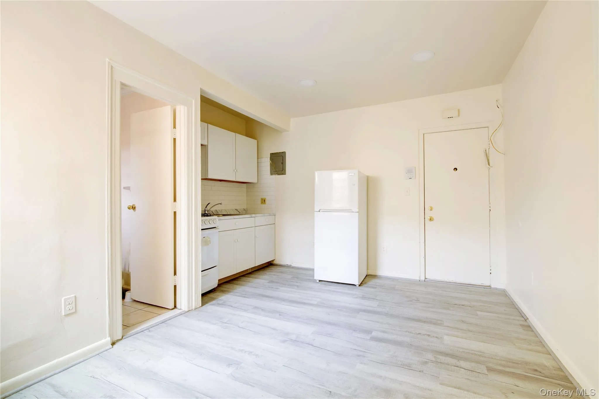 Kitchen with backsplash, white appliances, light wood-style flooring, white cabinetry, and light countertops Kitchen with backsplash, white appliances, light wood-style flooring, white cabinetry, and light countertops