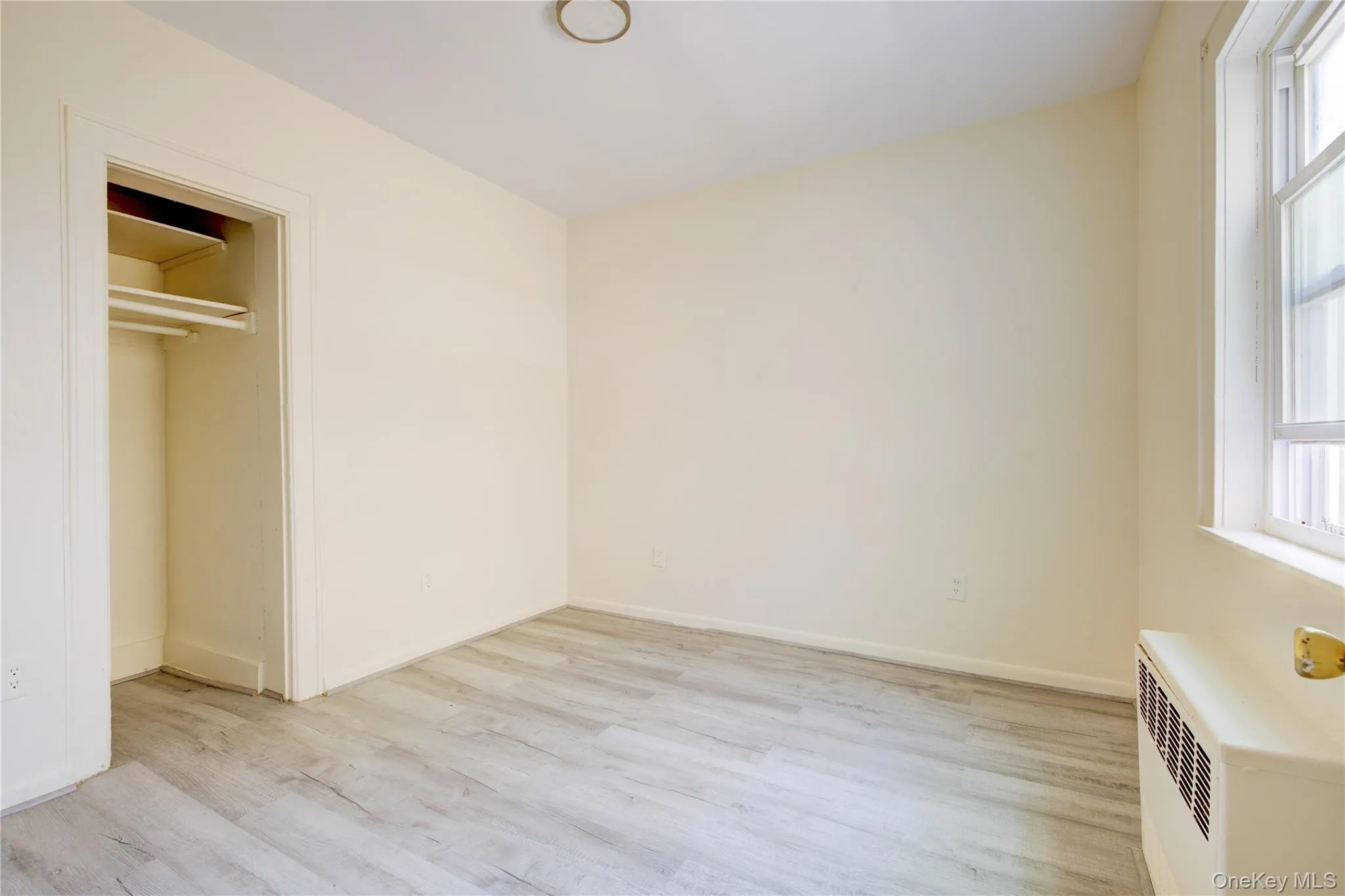Unfurnished bedroom with light wood finished floors, multiple windows, and radiator heating unit Unfurnished bedroom with light wood finished floors, multiple windows, and radiator heating unit