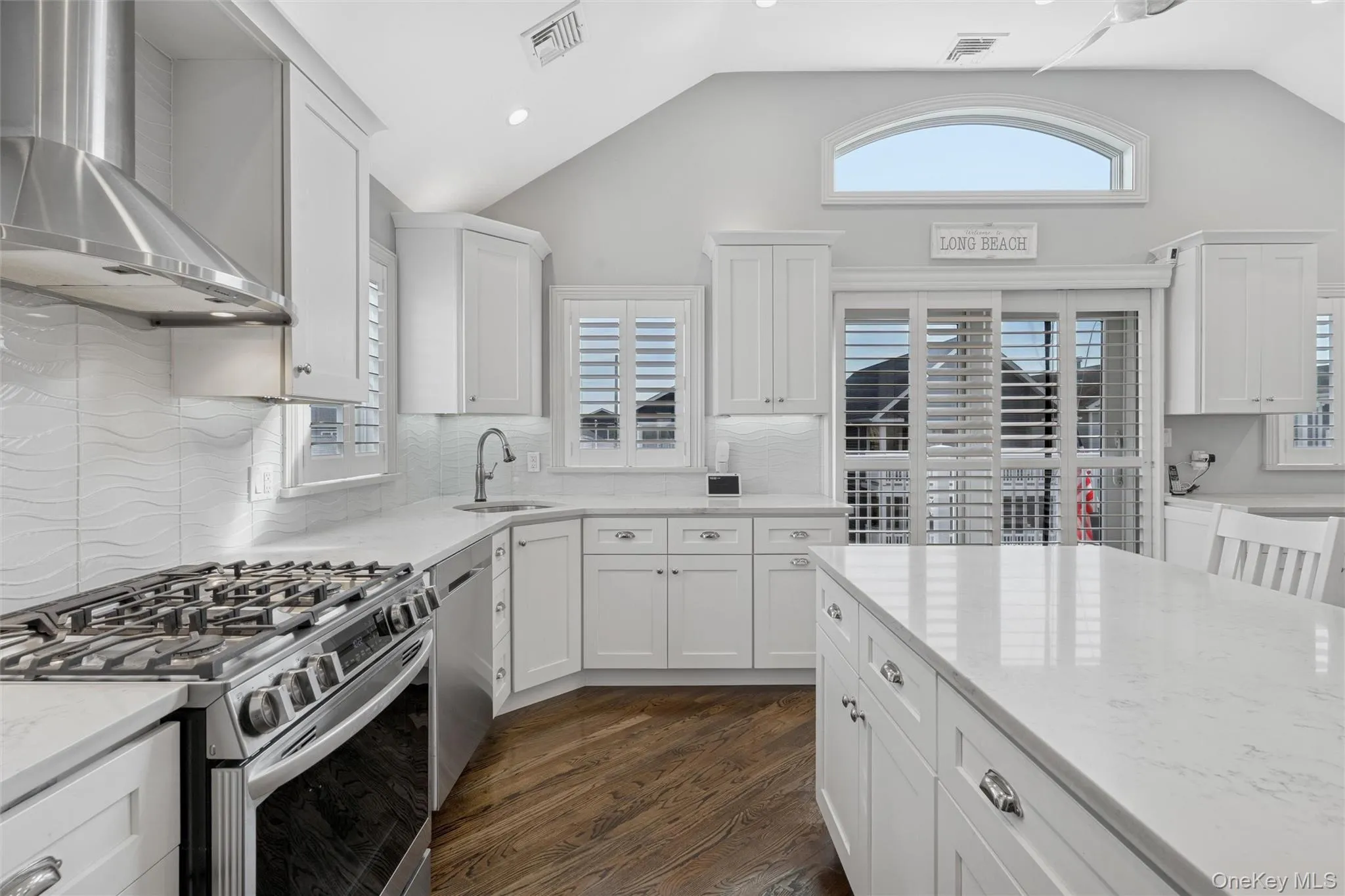 Kitchen with appliances with stainless steel finishes, wall chimney exhaust hood, white cabinets, light stone countertops, and dark wood-type flooring Kitchen with appliances with stainless steel finishes, wall chimney exhaust hood, white cabinets, light stone countertops, and dark wood-type flooring