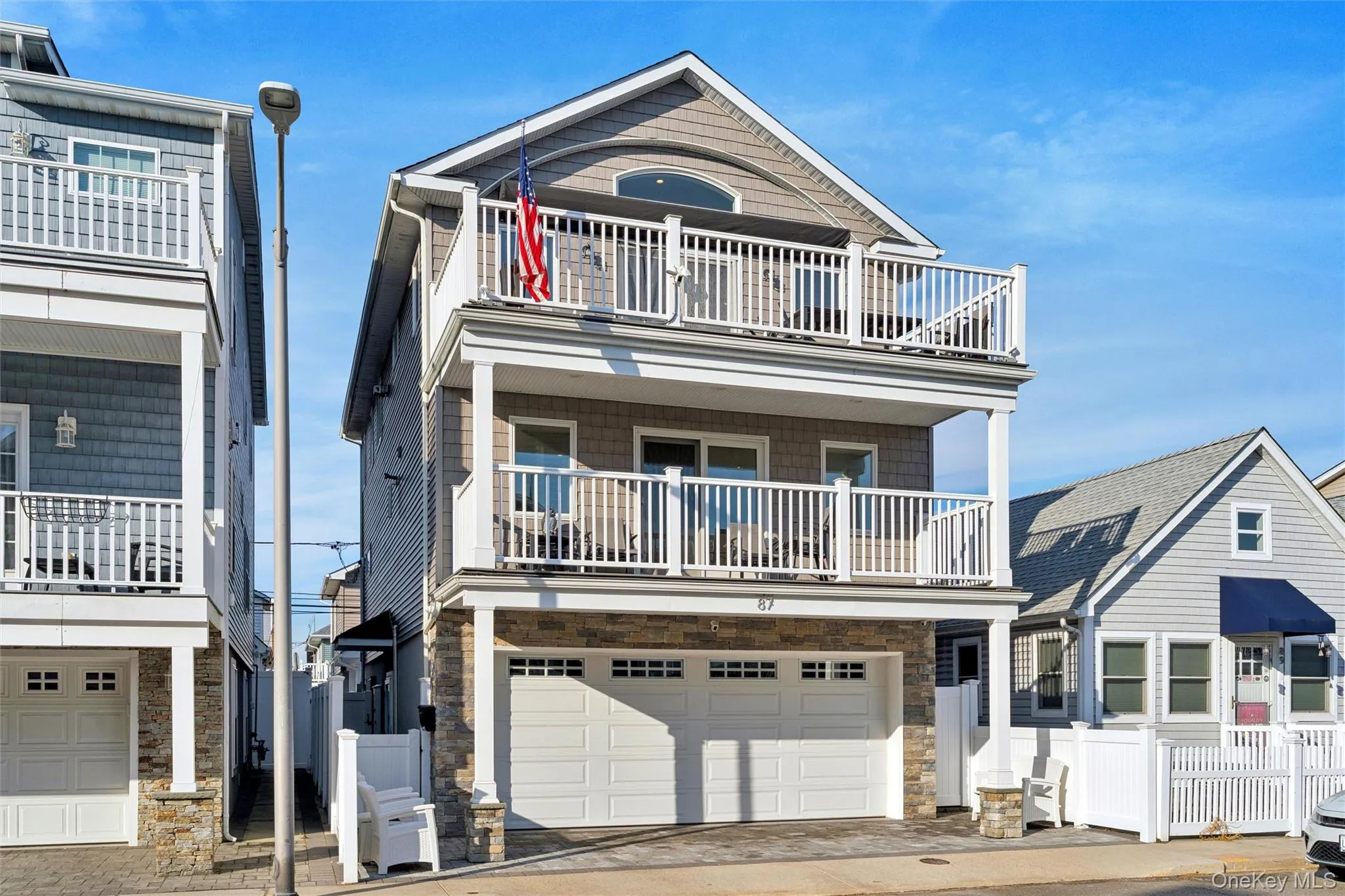 View of front facade featuring stone siding, a balcony, an attached garage, and driveway View of front facade featuring stone siding, a balcony, an attached garage, and driveway