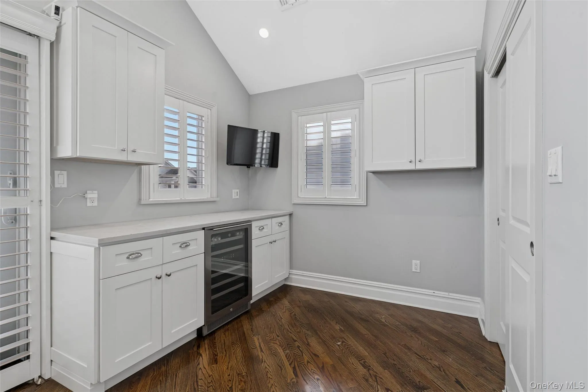 Kitchen featuring white cabinets, light countertops, beverage cooler, lofted ceiling, and dark wood finished floors Kitchen featuring white cabinets, light countertops, beverage cooler, lofted ceiling, and dark wood finished floors