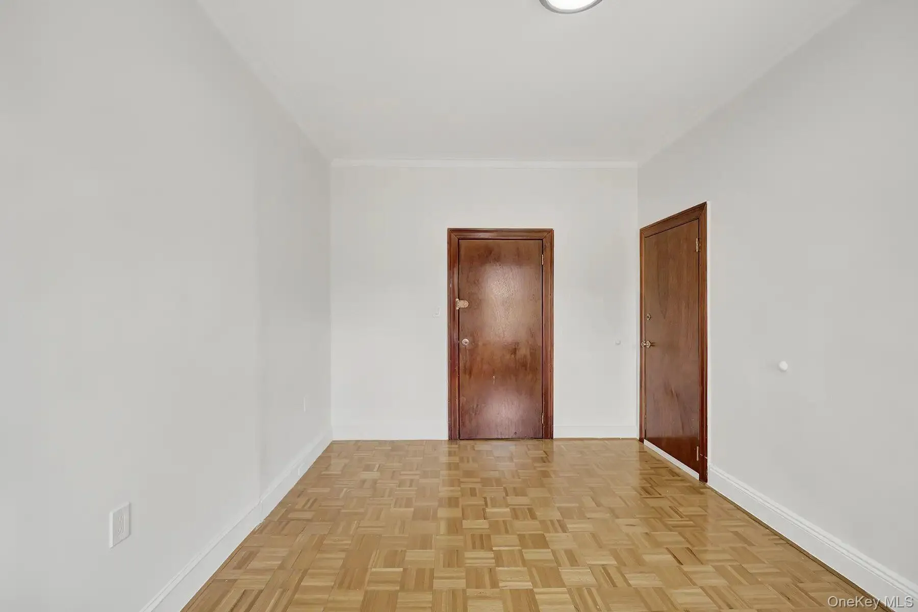 Spacious room with parquet flooring, white walls, and two wood-paneled doors Spacious room with parquet flooring, white walls, and two wood-paneled doors
