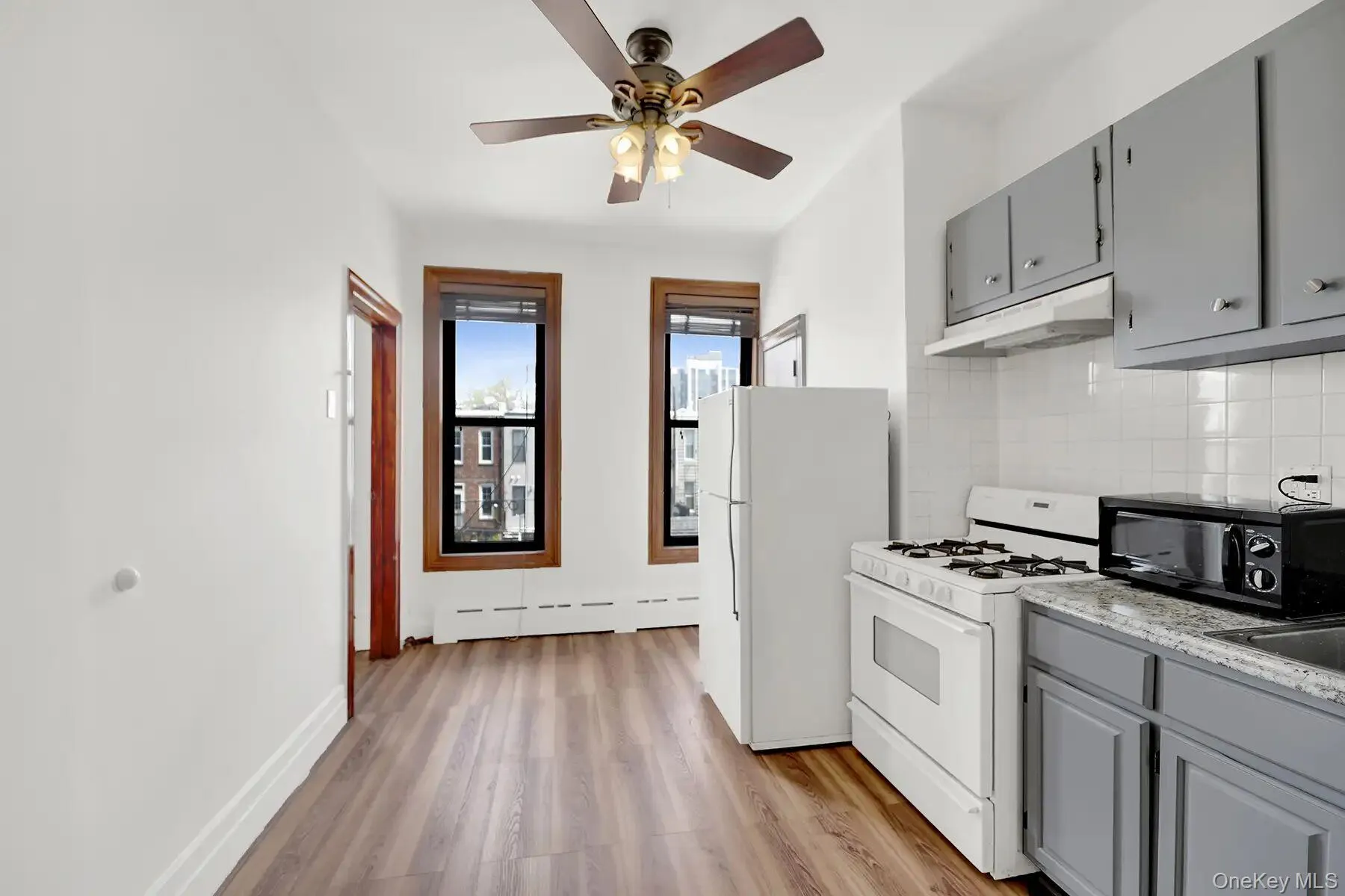Combined kitchen and living area featuring wood-finish flooring, white walls, and a ceiling fan with light fixture Combined kitchen and living area featuring wood-finish flooring, white walls, and a ceiling fan with light fixture