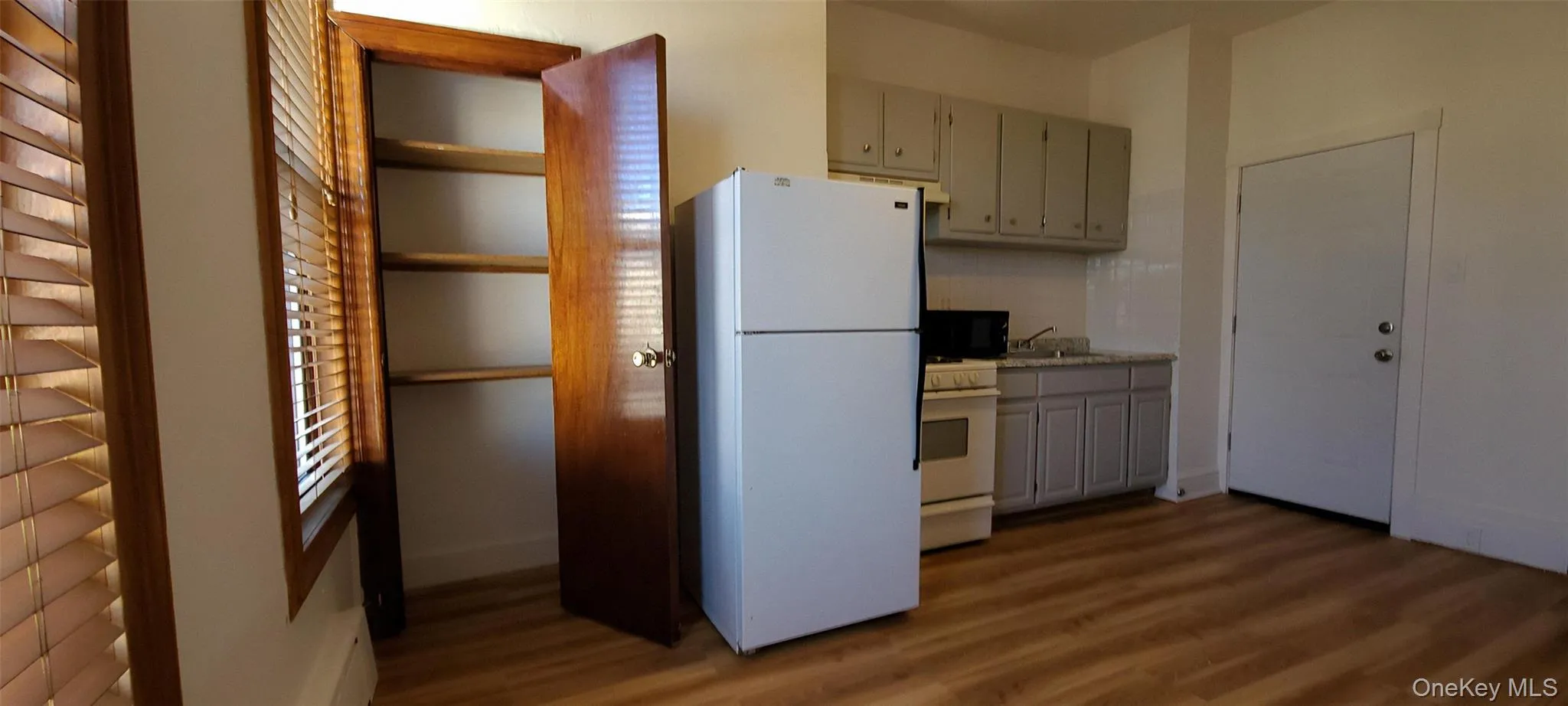 Kitchen featuring white appliances, gray cabinets, dark wood-style flooring, light countertops, and a baseboard heating unit Kitchen featuring white appliances, gray cabinets, dark wood-style flooring, light countertops, and a baseboard heating unit