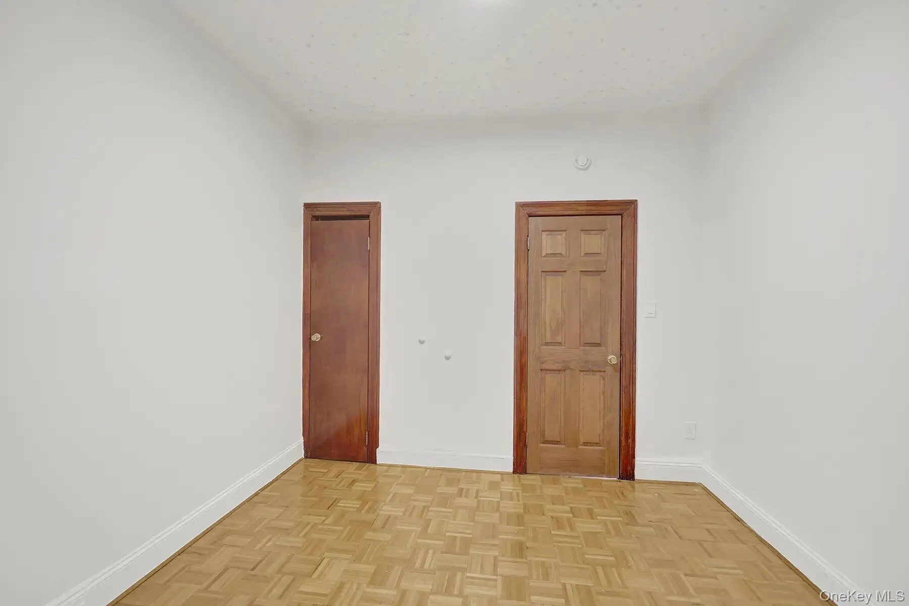 Room featuring light-toned parquet flooring, white wall finishes, and a baseboard trim Room featuring light-toned parquet flooring, white wall finishes, and a baseboard trim