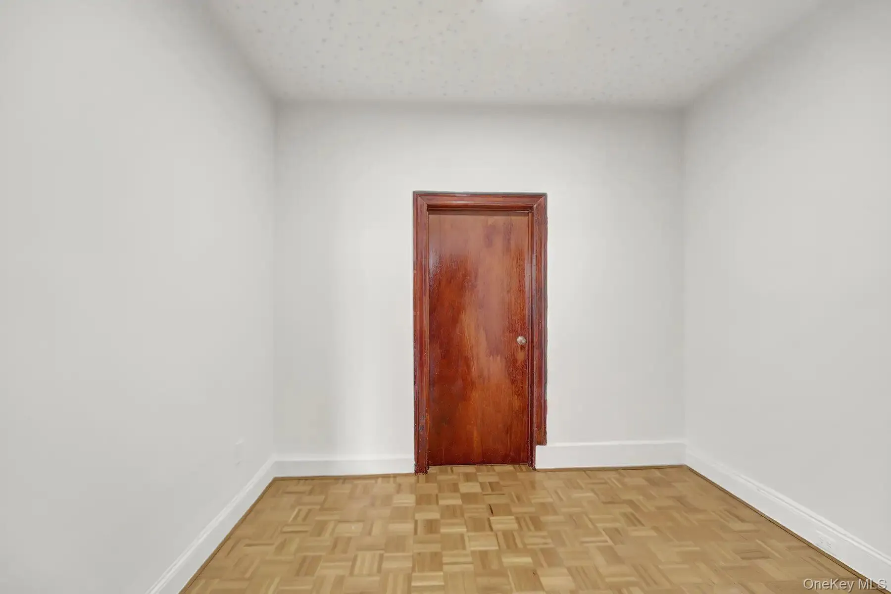 Room with parquet wood-finish flooring, white painted walls, and a recessed ceiling light Room with parquet wood-finish flooring, white painted walls, and a recessed ceiling light