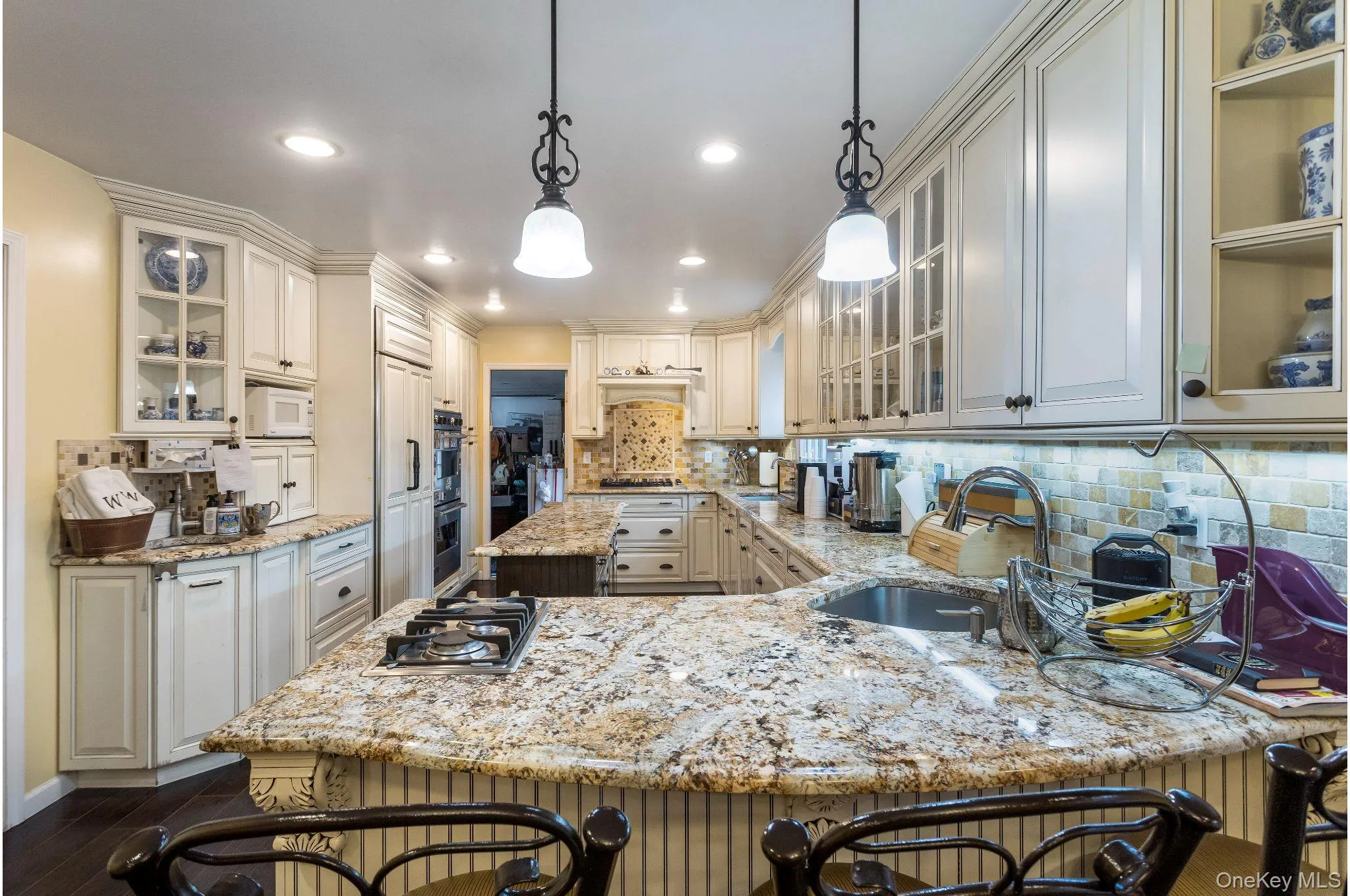 Kitchen featuring glass insert cabinets, a kitchen breakfast bar, backsplash, hanging light fixtures, and recessed lighting Kitchen featuring glass insert cabinets, a kitchen breakfast bar, backsplash, hanging light fixtures, and recessed lighting