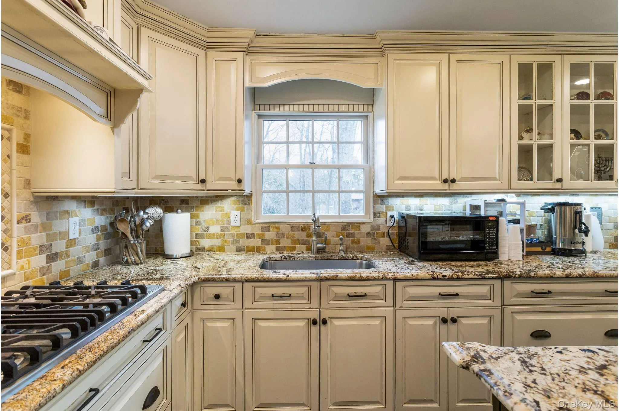 Kitchen with cream cabinets, stainless steel gas cooktop, light stone counters, and custom exhaust hood Kitchen with cream cabinets, stainless steel gas cooktop, light stone counters, and custom exhaust hood