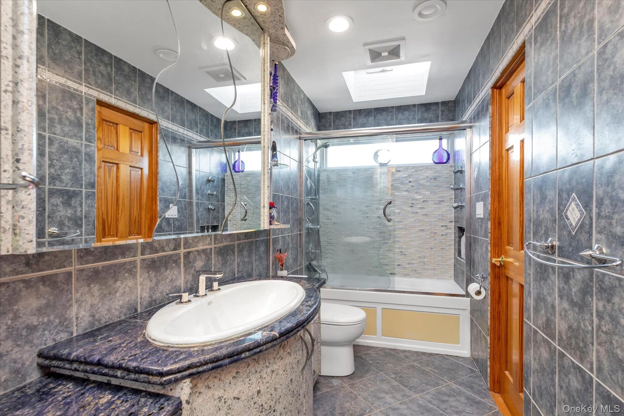 Bathroom featuring vanity, a combined bath / shower with rainfall shower, tile walls, and toilet Bathroom featuring vanity, a combined bath / shower with rainfall shower, tile walls, and toilet
