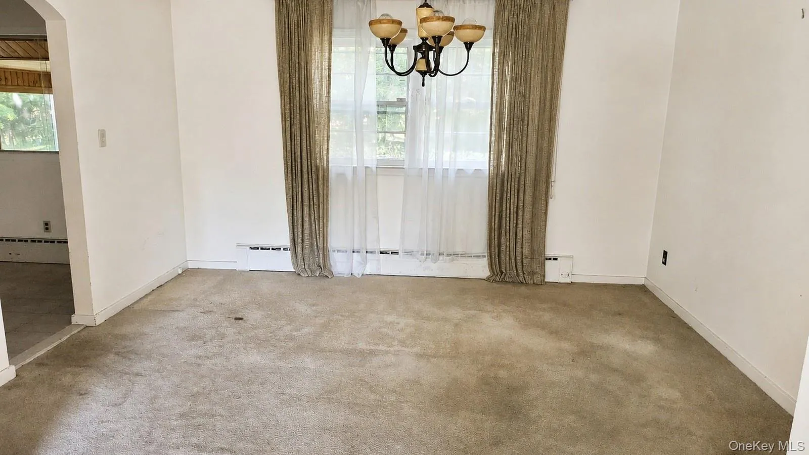 real estate listing photo of the dining room at 9 Sheep Pasture Lane in Huntington, NY, 11743, showing the chandelier, window, curtains, and visible carpet condition. real estate listing photo of the dining room at 9 Sheep Pasture Lane in Huntington, NY, 11743, showing the chandelier, window, curtains, and visible carpet condition.