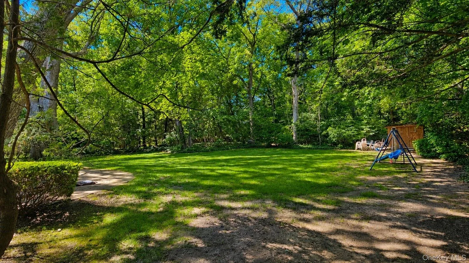 real estate listing photo showing the backyard lawn, mature trees, shaded outdoor space, and swing set at 9 Sheep Pasture Lane in Huntington, NY, 11743. real estate listing photo showing the backyard lawn, mature trees, shaded outdoor space, and swing set at 9 Sheep Pasture Lane in Huntington, NY, 11743.
