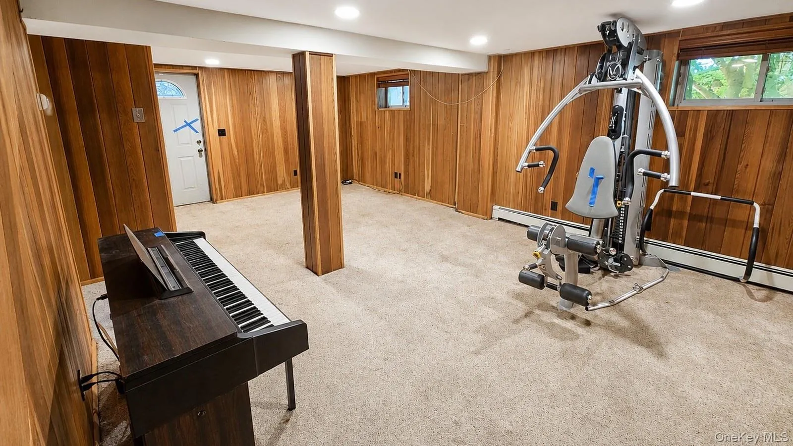 real estate listing photo of the finished basement at 9 Sheep Pasture Lane in Huntington, NY, showing wood-paneled walls, carpet, piano, and exercise equipment. real estate listing photo of the finished basement at 9 Sheep Pasture Lane in Huntington, NY, showing wood-paneled walls, carpet, piano, and exercise equipment.