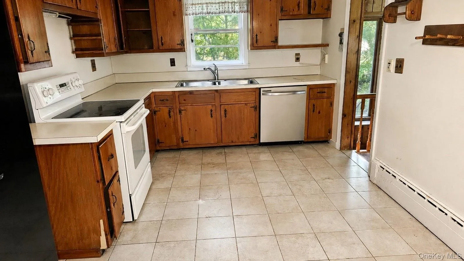 real estate listing photo showing the eat-in kitchen at 9 Sheep Pasture Lane in Huntington, NY 11743 with wood cabinetry, tile floor, white stove, stainless dishwasher, and side door. real estate listing photo showing the eat-in kitchen at 9 Sheep Pasture Lane in Huntington, NY 11743 with wood cabinetry, tile floor, white stove, stainless dishwasher, and side door.