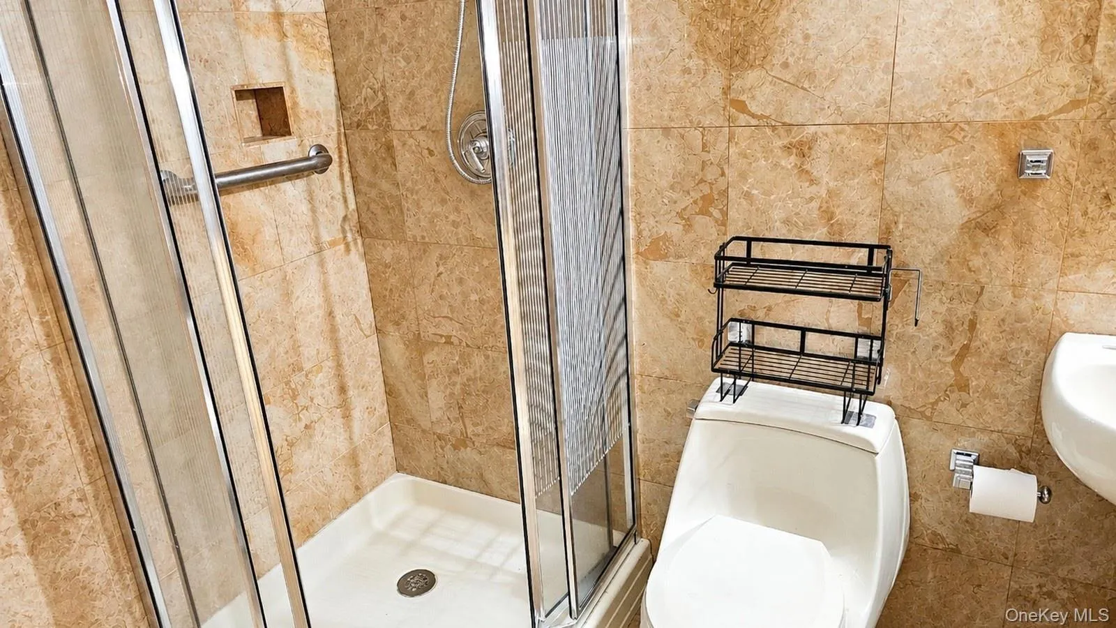 Tiled shower enclosure featuring a glass door, grab bar, built-in shelf, and a white shower pan Tiled shower enclosure featuring a glass door, grab bar, built-in shelf, and a white shower pan