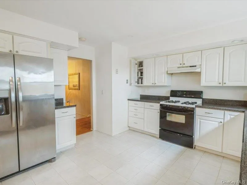 Kitchen with stainless steel fridge, range with gas stovetop, white cabinets, under cabinet range hood, and open shelves Kitchen with stainless steel fridge, range with gas stovetop, white cabinets, under cabinet range hood, and open shelves