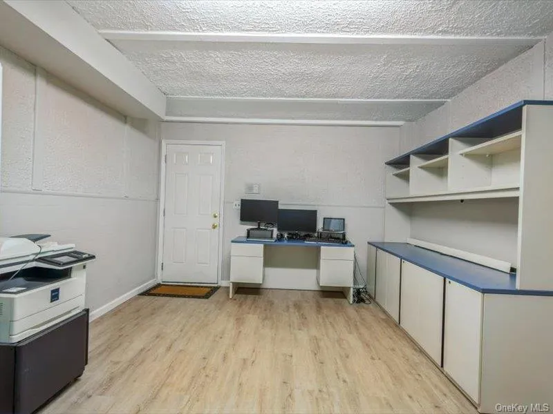 Kitchen with a desk, light wood-style flooring, dark countertops, a textured ceiling, and white cabinetry Kitchen with a desk, light wood-style flooring, dark countertops, a textured ceiling, and white cabinetry
