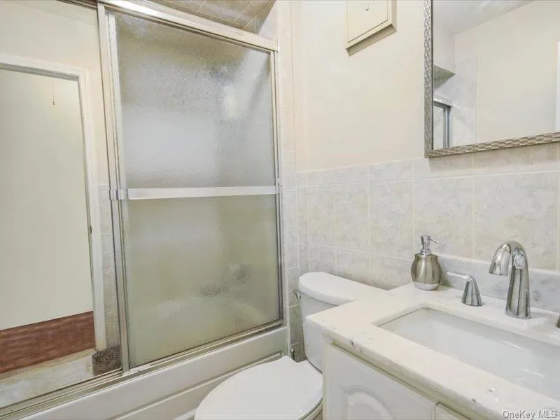 Full bathroom featuring vanity, tile walls, and shower / bath combination with glass door Full bathroom featuring vanity, tile walls, and shower / bath combination with glass door