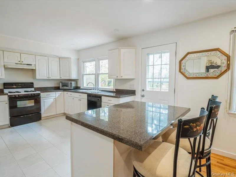Kitchen featuring range with gas cooktop, white cabinets, a breakfast bar area, dark stone counters, and a kitchen island Kitchen featuring range with gas cooktop, white cabinets, a breakfast bar area, dark stone counters, and a kitchen island