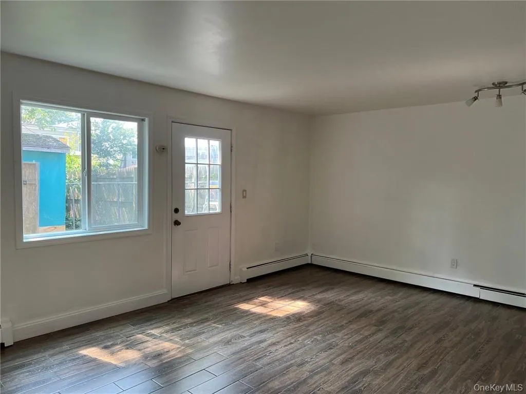 Part of living room/dining area with a door to the backyard. Baseboard heating and dark hardwood / wood-style floors Part of living room/dining area with a door to the backyard. Baseboard heating and dark hardwood / wood-style floors