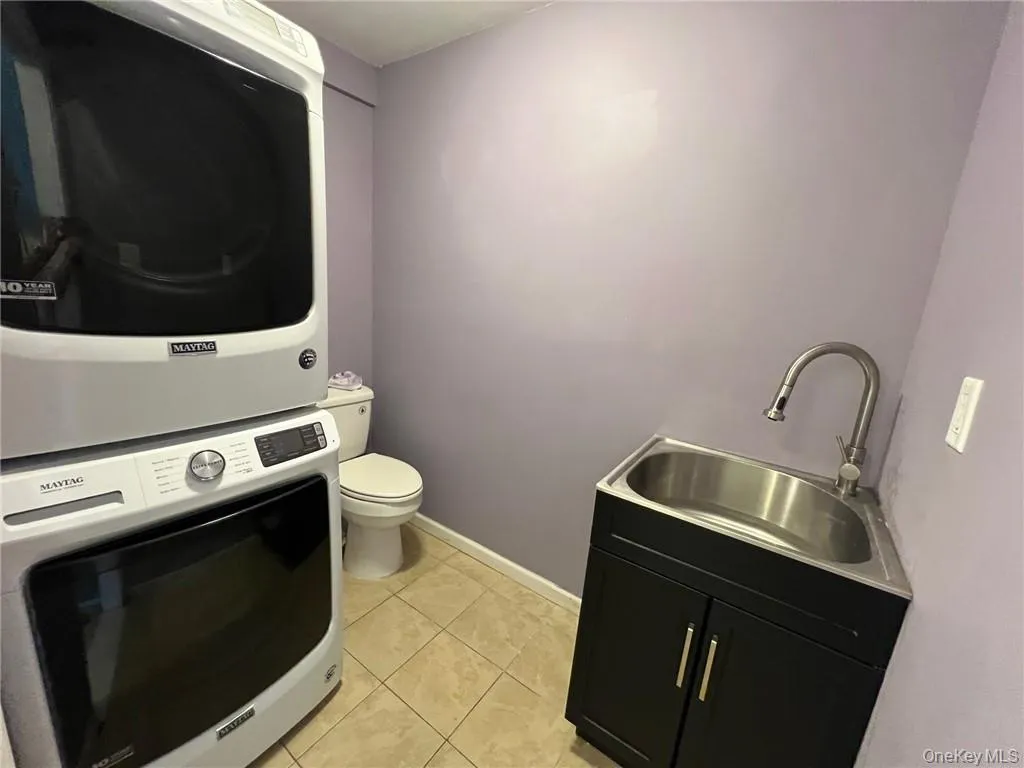 Laundry room and half bath combination with light tile patterned floors, sink, and stacked washer / drying machine Laundry room and half bath combination with light tile patterned floors, sink, and stacked washer / drying machine
