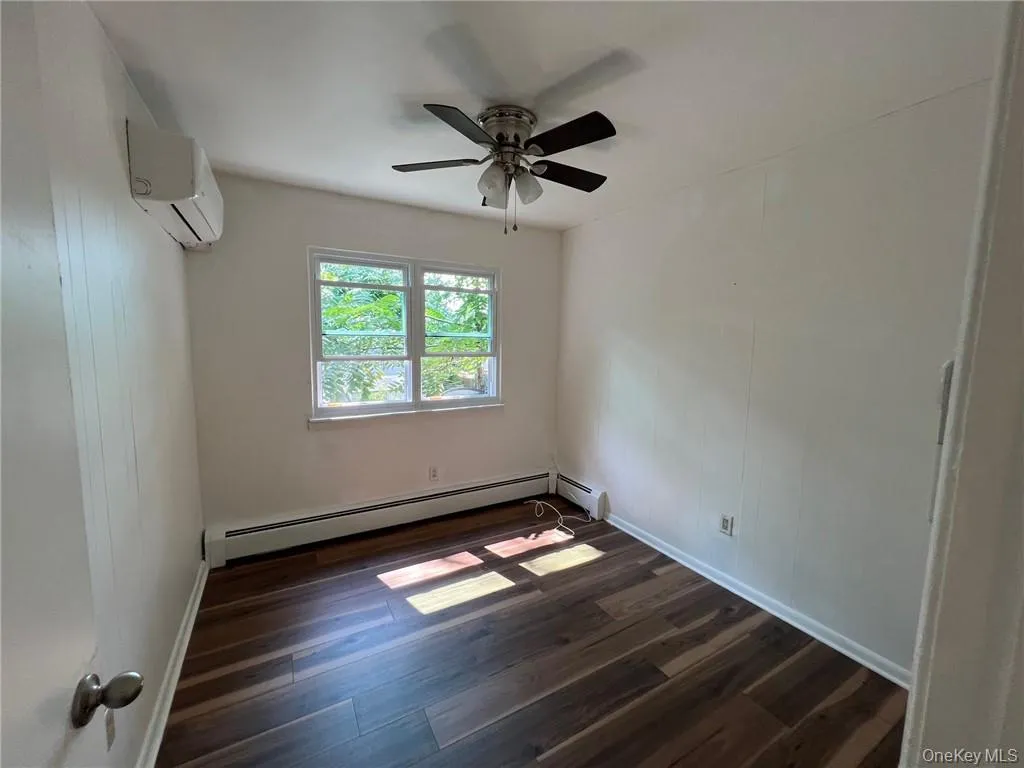 Bedroom #3 with dark wood-type flooring, a baseboard radiator, a wall mounted air conditioner, and ceiling fan Bedroom #3 with dark wood-type flooring, a baseboard radiator, a wall mounted air conditioner, and ceiling fan