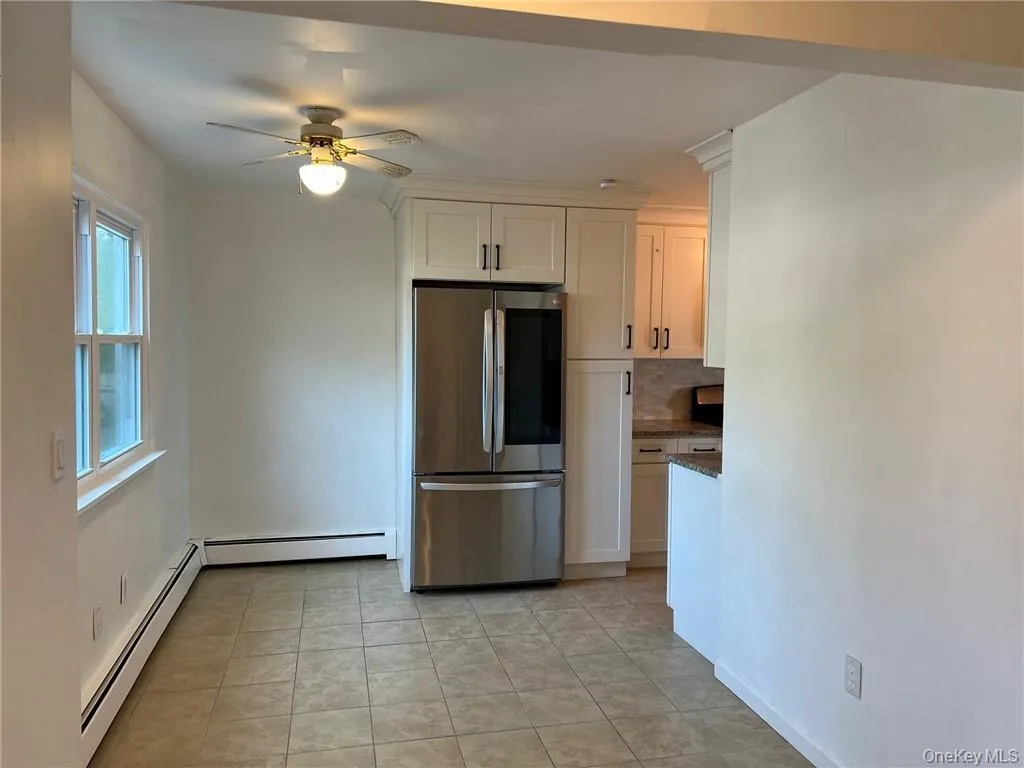 Kitchen and small dining area with a baseboard heating, ceiling fan, stainless steel refrigerator, and white cabinets Kitchen and small dining area with a baseboard heating, ceiling fan, stainless steel refrigerator, and white cabinets