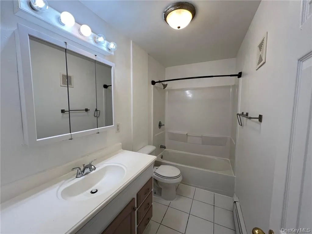 Full bathroom with toilet, tile patterned floors, vanity, baseboard heating, and bathing tub / shower combination Full bathroom with toilet, tile patterned floors, vanity, baseboard heating, and bathing tub / shower combination