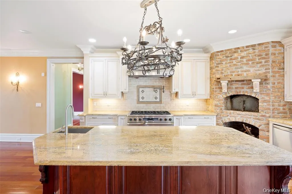 Kitchen featuring crown molding, a kitchen island, tasteful backsplash, light stone countertops, and decorative light fixtures Kitchen featuring crown molding, a kitchen island, tasteful backsplash, light stone countertops, and decorative light fixtures