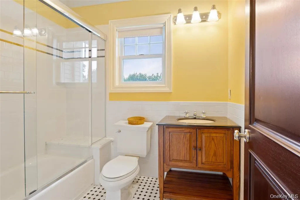 Full bathroom featuring vanity, tile walls, a wainscoted wall, combined bath / shower with glass door, and dark tile patterned floors Full bathroom featuring vanity, tile walls, a wainscoted wall, combined bath / shower with glass door, and dark tile patterned floors