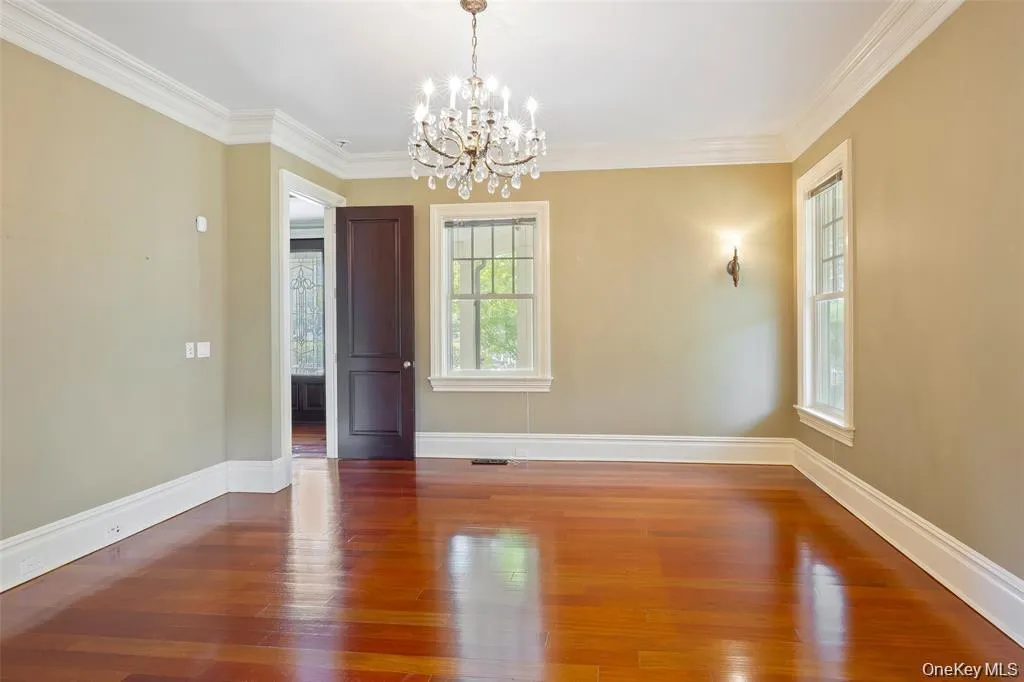 Empty room featuring ornamental molding, wood finished floors, and a chandelier Empty room featuring ornamental molding, wood finished floors, and a chandelier