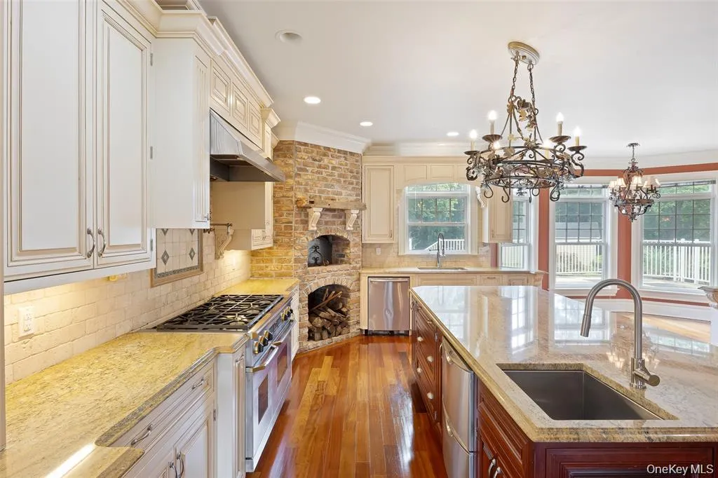Kitchen with backsplash, light stone counters, hanging light fixtures, appliances with stainless steel finishes, and dark wood finished floors Kitchen with backsplash, light stone counters, hanging light fixtures, appliances with stainless steel finishes, and dark wood finished floors