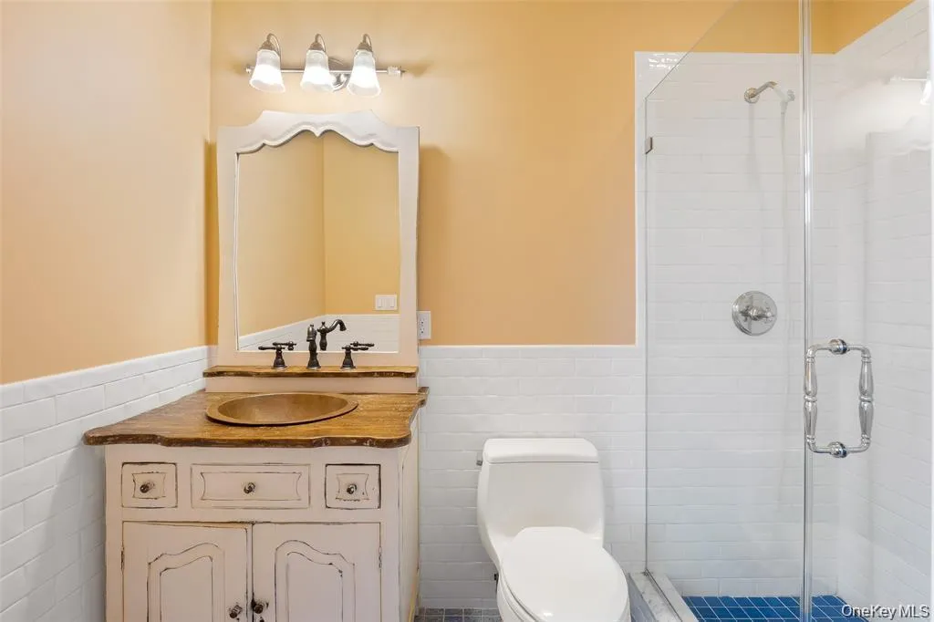 Bathroom with tile walls, a wainscoted wall, vanity, and a shower stall Bathroom with tile walls, a wainscoted wall, vanity, and a shower stall