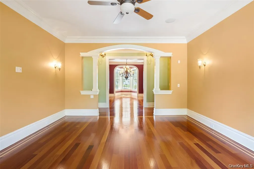 Spare room with hardwood / wood-style floors, crown molding, arched walkways, a chandelier, and decorative columns Spare room with hardwood / wood-style floors, crown molding, arched walkways, a chandelier, and decorative columns
