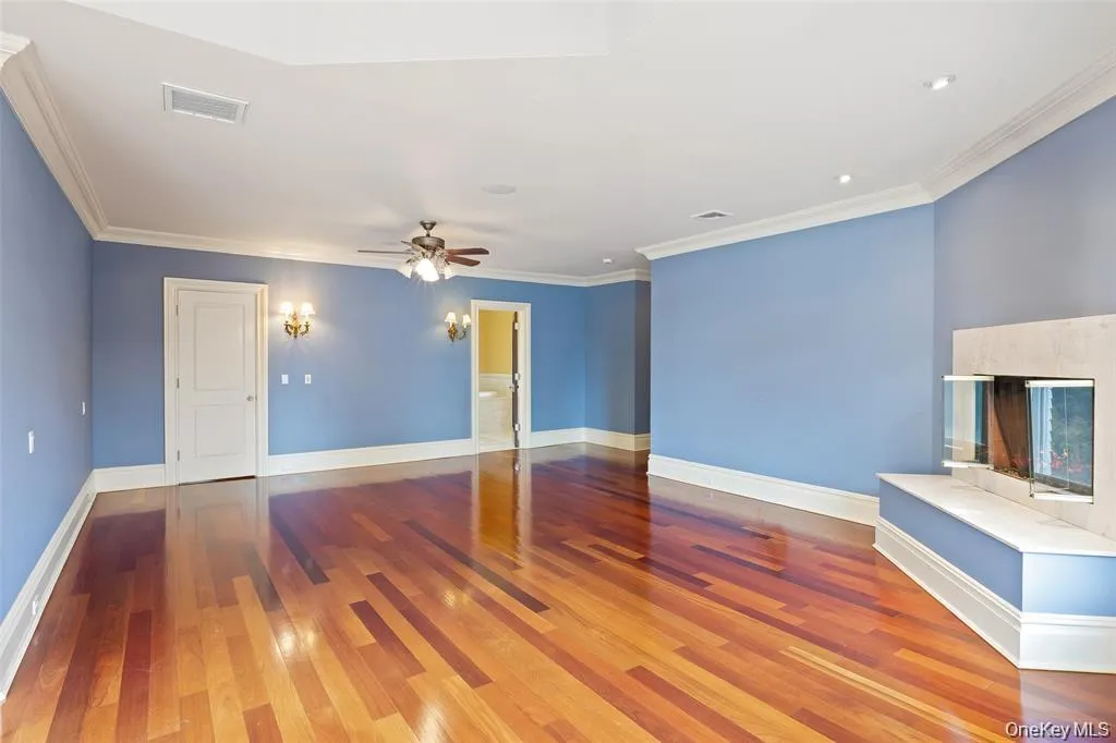 Unfurnished living room with dark wood-type flooring, ornamental molding, ceiling fan, and a fireplace Unfurnished living room with dark wood-type flooring, ornamental molding, ceiling fan, and a fireplace