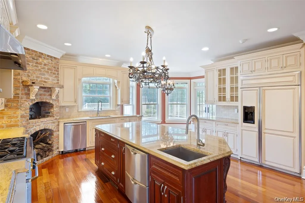 Kitchen featuring decorative backsplash, glass insert cabinets, stainless steel appliances, light stone countertops, and decorative light fixtures Kitchen featuring decorative backsplash, glass insert cabinets, stainless steel appliances, light stone countertops, and decorative light fixtures