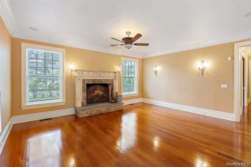 Unfurnished living room featuring hardwood / wood-style floors, ceiling fan, ornamental molding, and a fireplace Unfurnished living room featuring hardwood / wood-style floors, ceiling fan, ornamental molding, and a fireplace