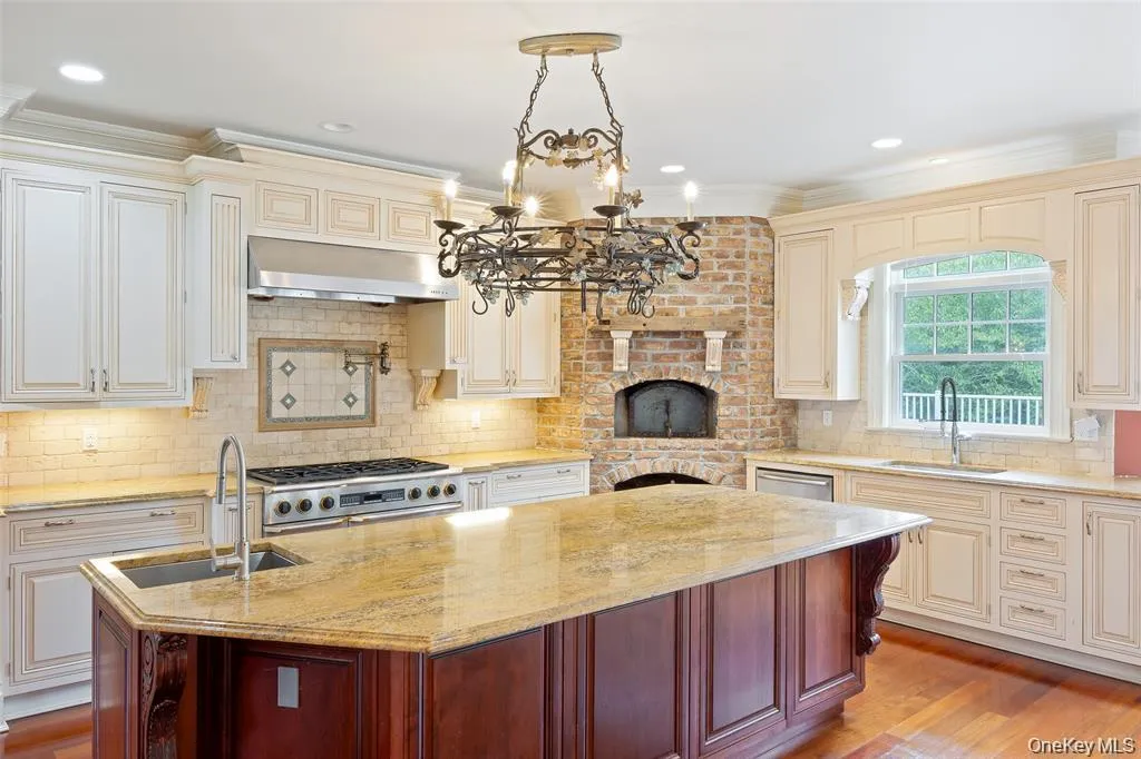 Kitchen featuring backsplash, cream cabinetry, light stone counters, light wood-style flooring, and hanging light fixtures Kitchen featuring backsplash, cream cabinetry, light stone counters, light wood-style flooring, and hanging light fixtures