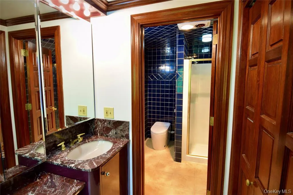 Full bathroom featuring vanity, light tile patterned flooring, a shower stall, and ornamental molding Full bathroom featuring vanity, light tile patterned flooring, a shower stall, and ornamental molding
