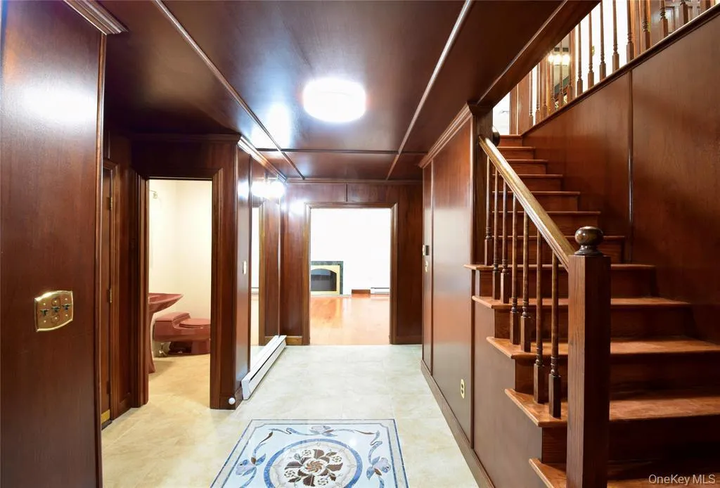Hallway with baseboard heating, wooden walls, ornamental molding, and stairs Hallway with baseboard heating, wooden walls, ornamental molding, and stairs