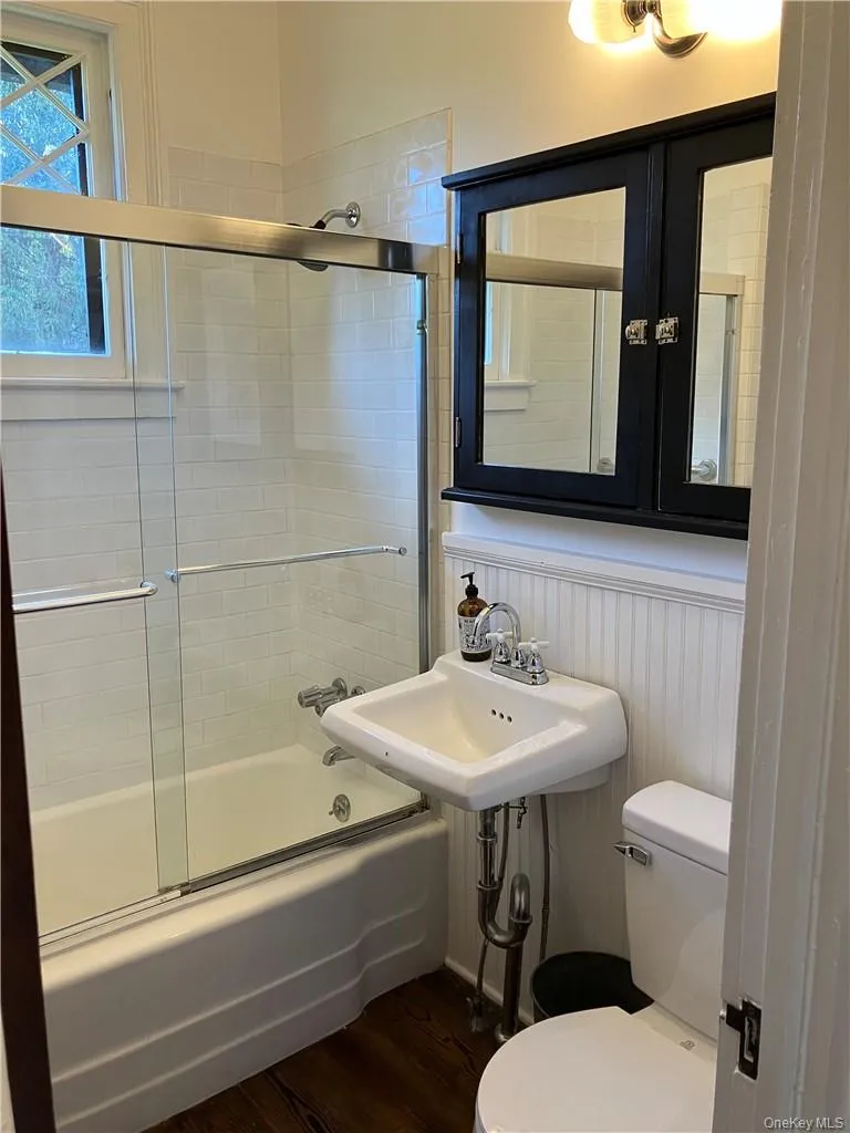 Bathroom with combined bath / shower with glass door, toilet, and wood-type flooring Bathroom with combined bath / shower with glass door, toilet, and wood-type flooring