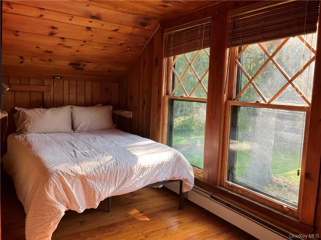 Bedroom featuring wooden walls, a baseboard heating unit, wood ceiling, lofted ceiling, and hardwood / wood-style flooring Bedroom featuring wooden walls, a baseboard heating unit, wood ceiling, lofted ceiling, and hardwood / wood-style flooring