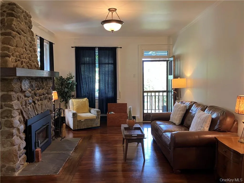 Living room featuring dark hardwood / wood-style flooring, crown molding, and a stone fireplace Living room featuring dark hardwood / wood-style flooring, crown molding, and a stone fireplace