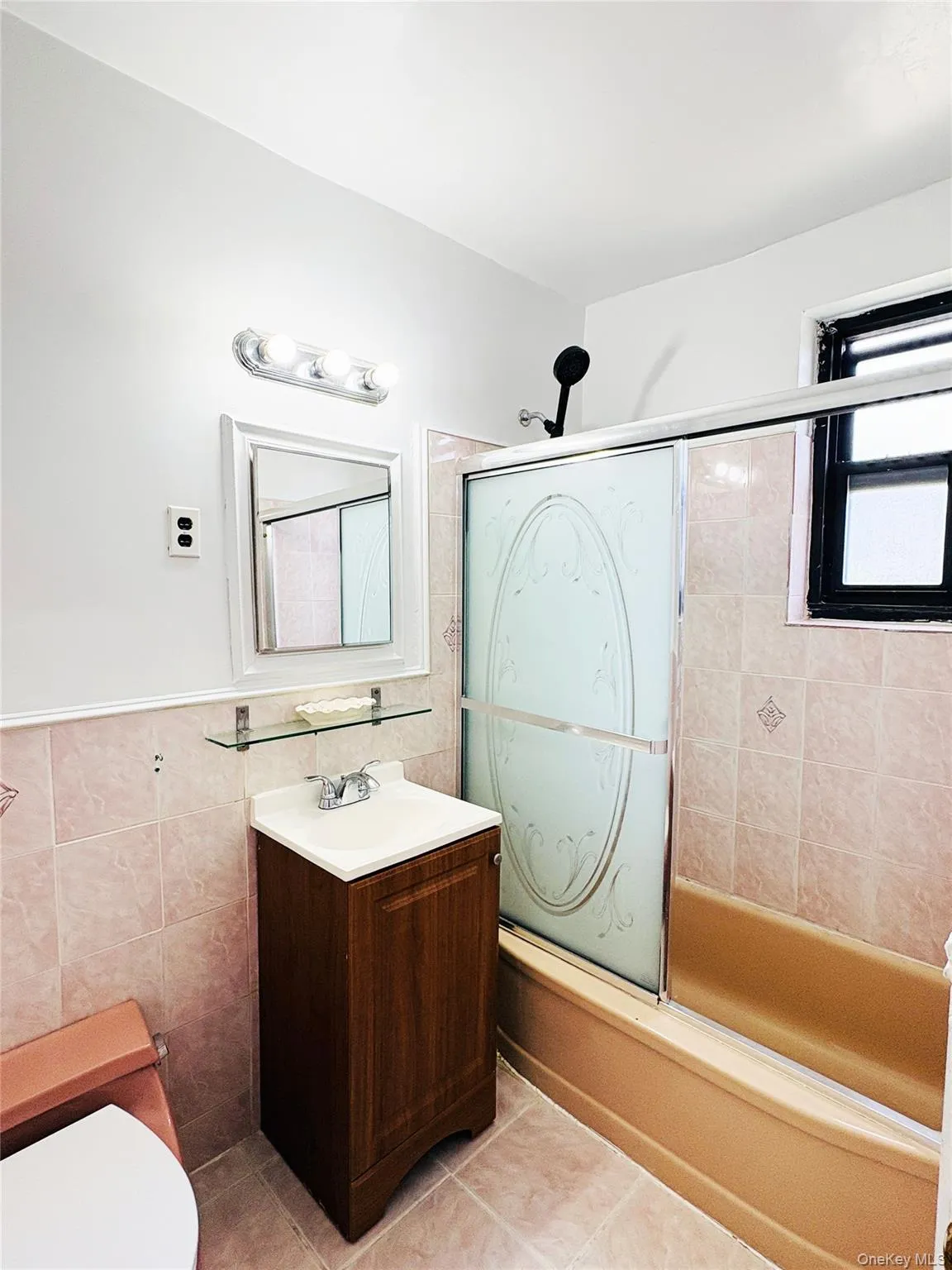 Bathroom featuring ceramic tile walls and flooring, a single vanity with a white countertop, a mirrored medicine cabinet, and a bathtub with a sliding glass enclosure Bathroom featuring ceramic tile walls and flooring, a single vanity with a white countertop, a mirrored medicine cabinet, and a bathtub with a sliding glass enclosure