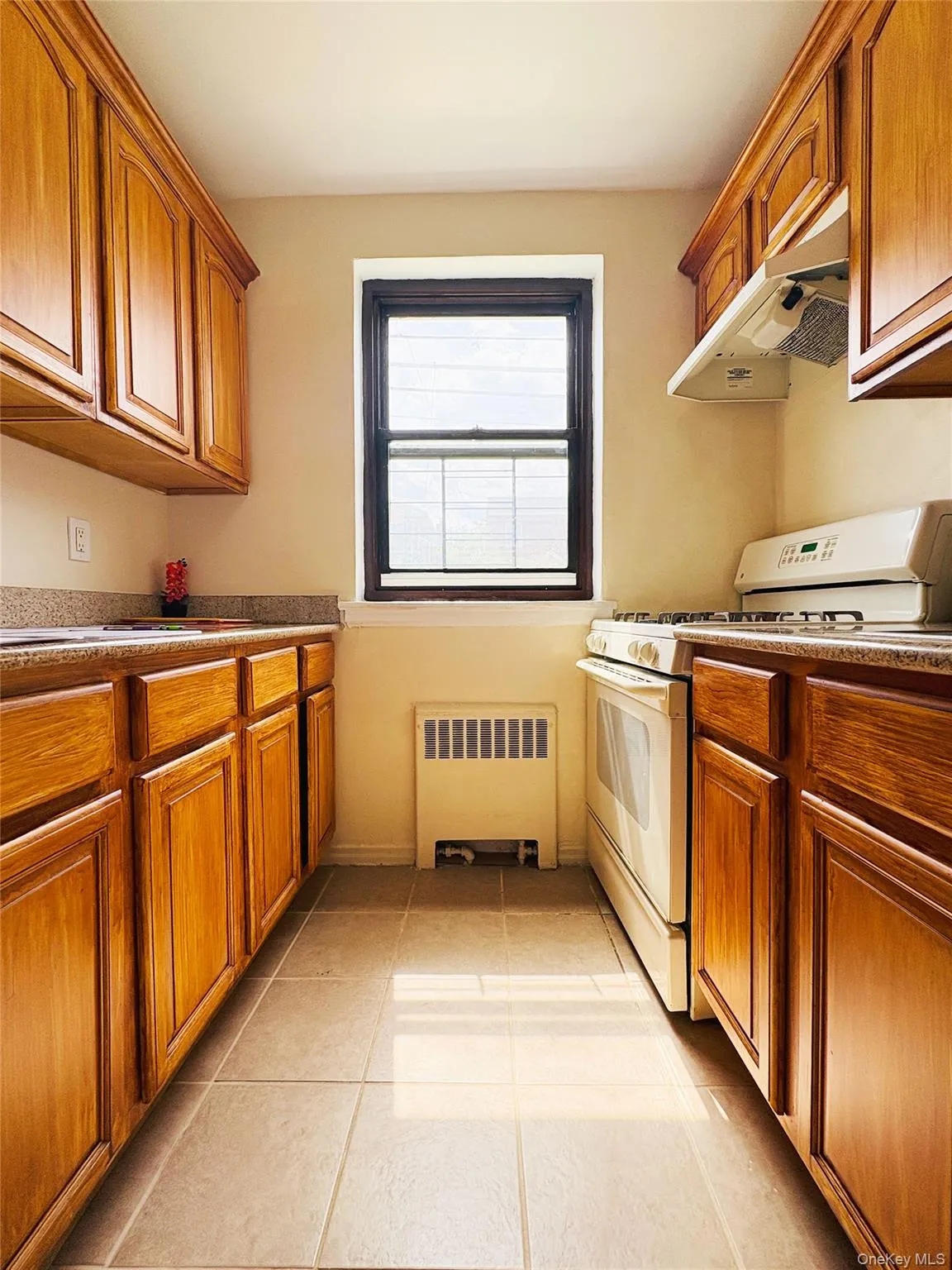 Galley kitchen featuring wood-finish cabinetry, light-toned countertops, and tile flooring Galley kitchen featuring wood-finish cabinetry, light-toned countertops, and tile flooring