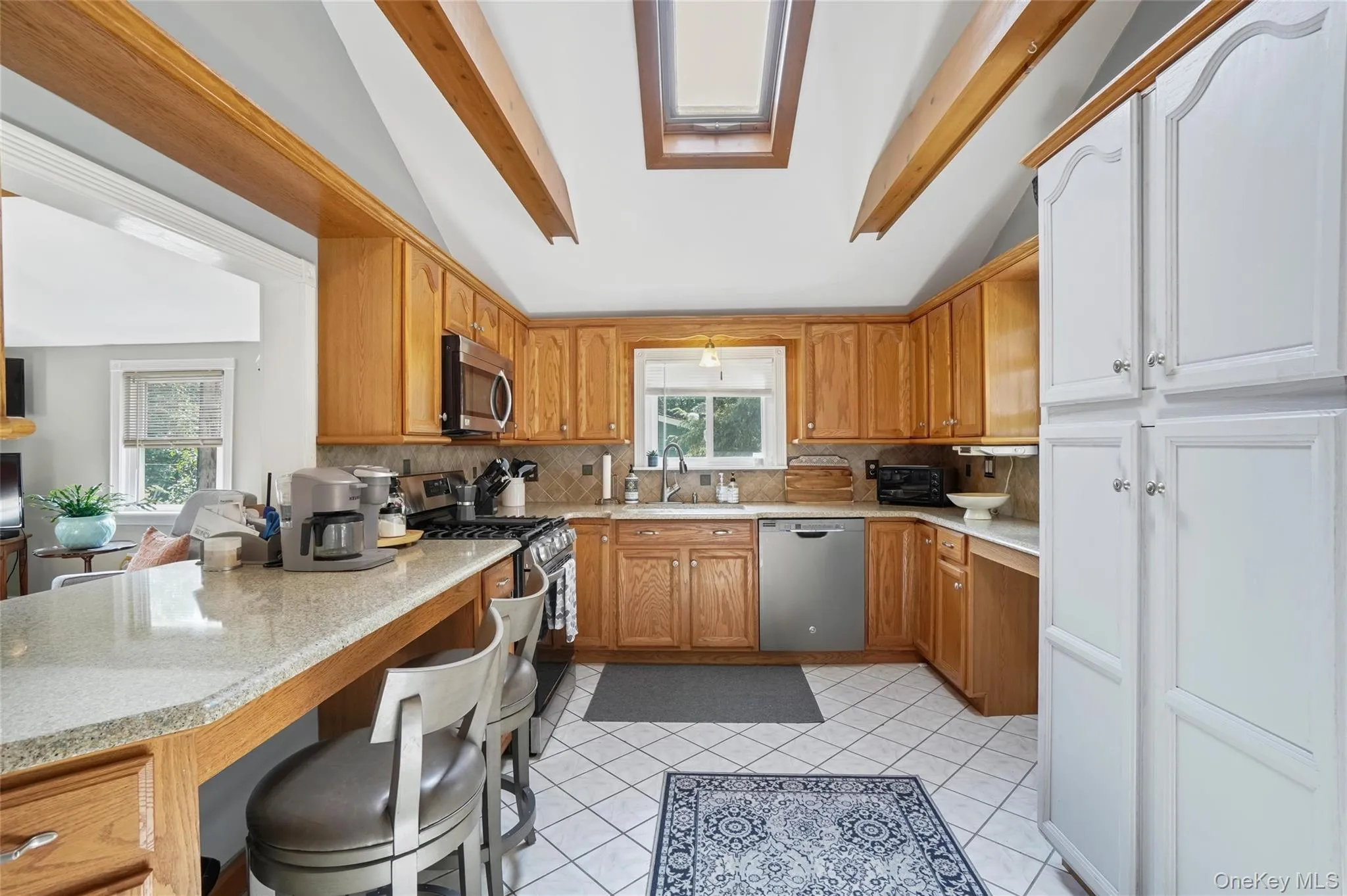 Kitchen with brown cabinets, stainless steel appliances, light tile patterned floors, tasteful backsplash, and light stone counters Kitchen with brown cabinets, stainless steel appliances, light tile patterned floors, tasteful backsplash, and light stone counters
