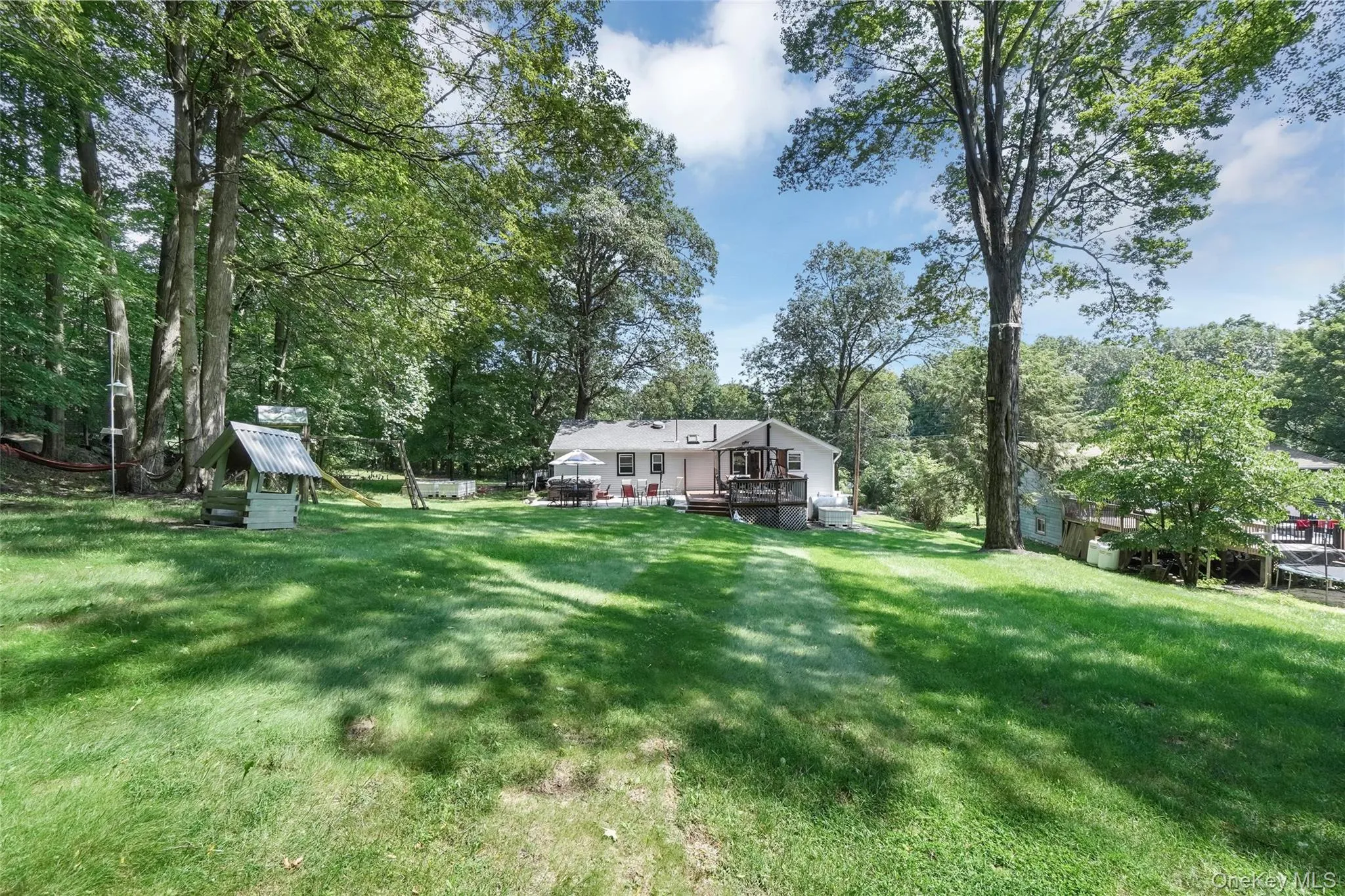 View of green lawn featuring a wooden deck and view of scattered trees View of green lawn featuring a wooden deck and view of scattered trees