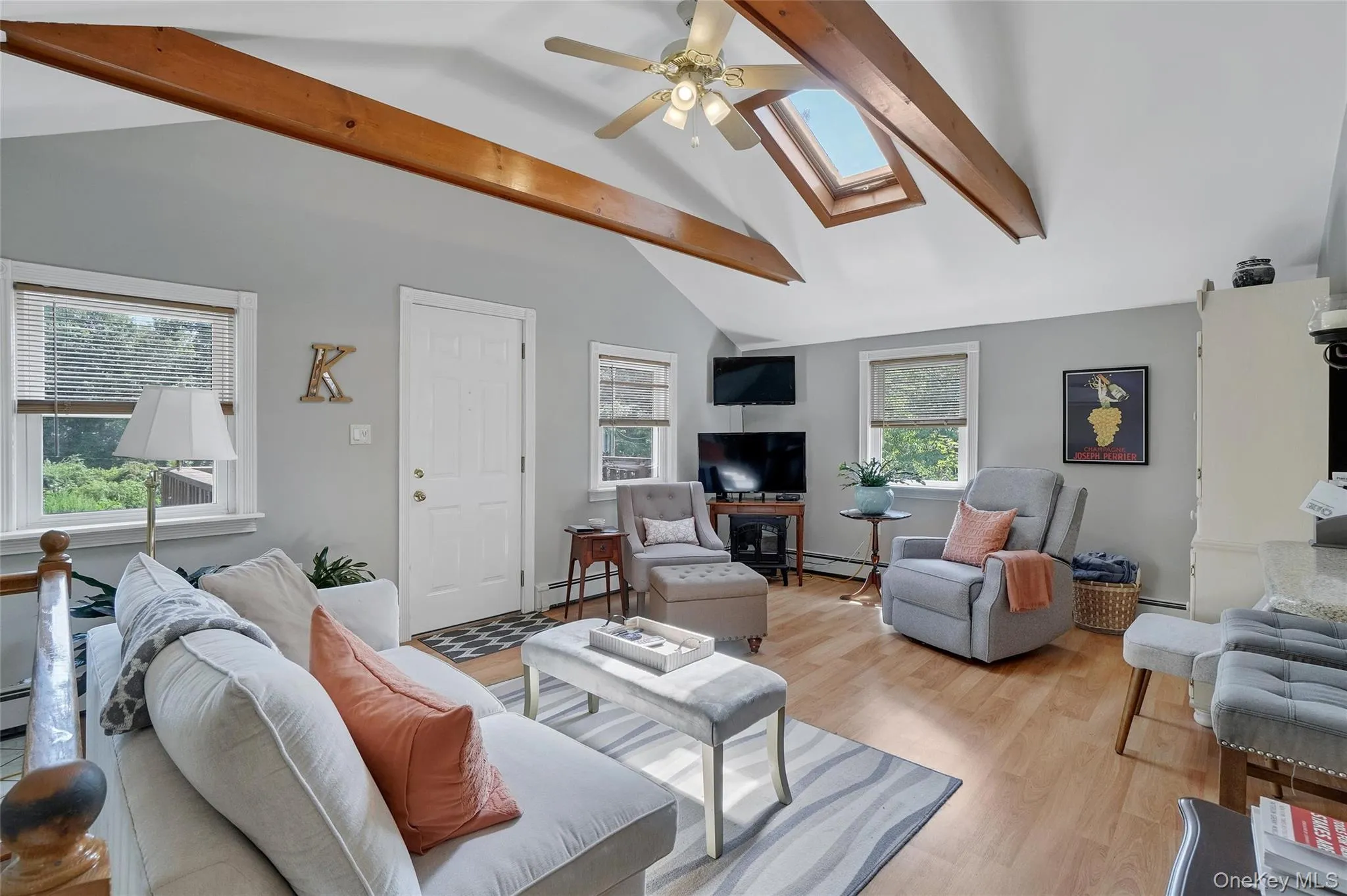 Living room with a skylight, beam ceiling, light wood-style floors, ceiling fan, and a baseboard radiator Living room with a skylight, beam ceiling, light wood-style floors, ceiling fan, and a baseboard radiator