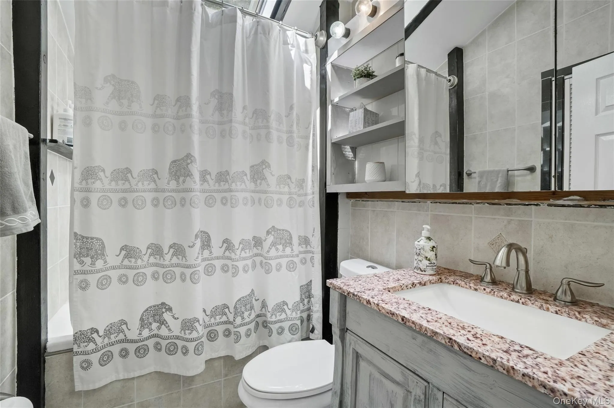 Full bathroom with tile walls, vanity, backsplash, and shower / bath combo with shower curtain Full bathroom with tile walls, vanity, backsplash, and shower / bath combo with shower curtain