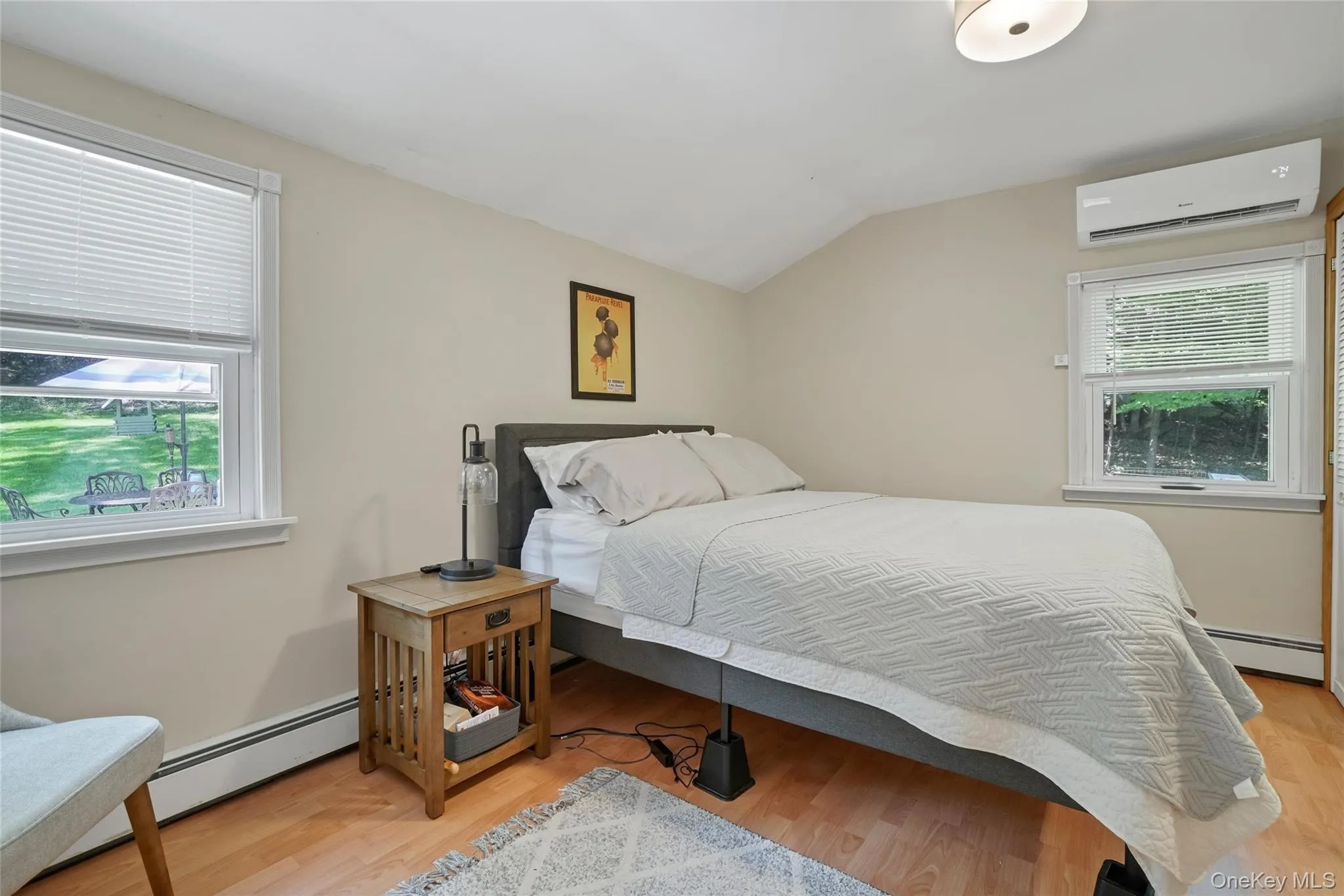 Bedroom featuring lofted ceiling, a wall unit AC, baseboard heating, and light wood-type flooring Bedroom featuring lofted ceiling, a wall unit AC, baseboard heating, and light wood-type flooring